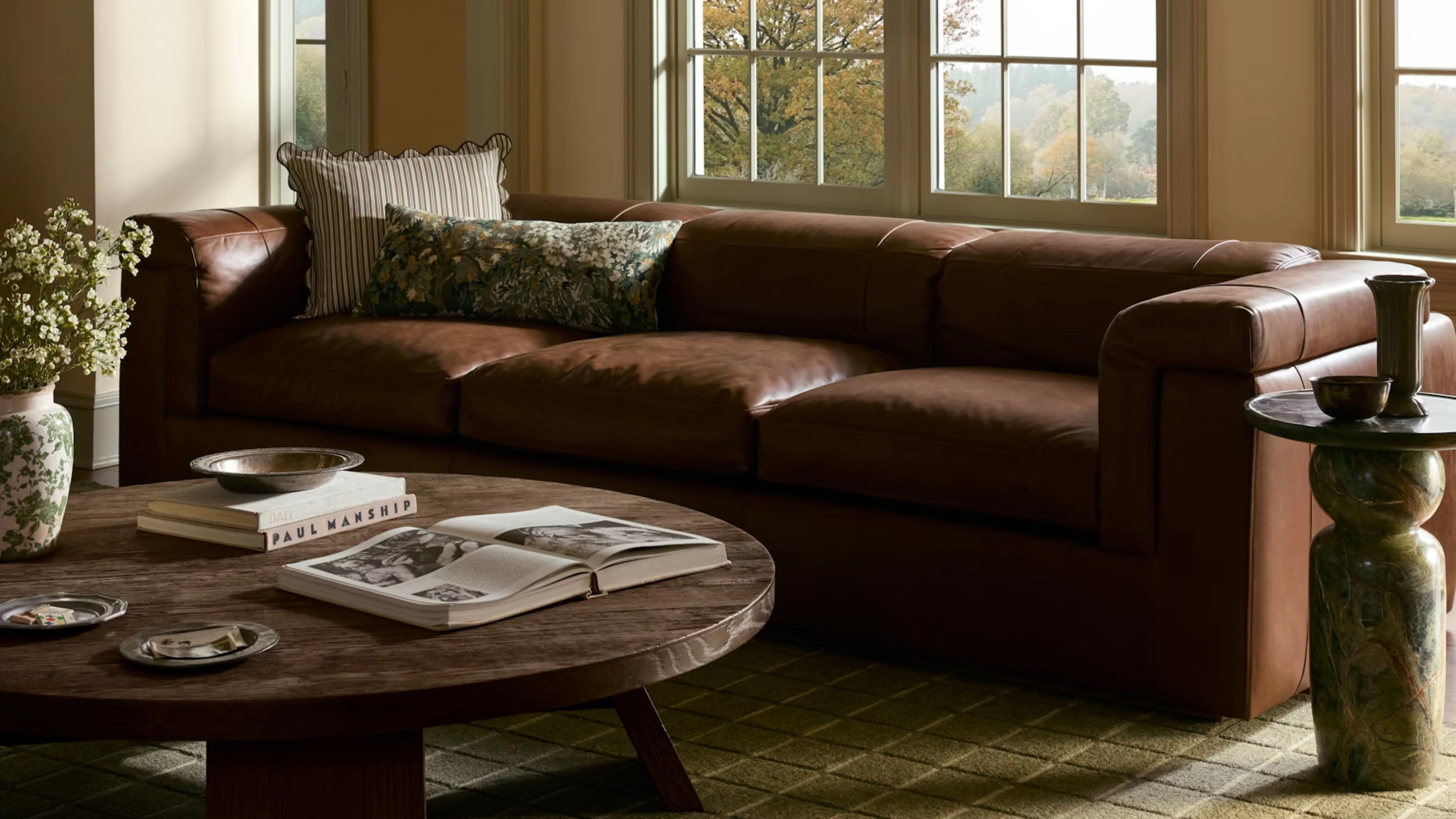 Herbstliche Kissenbezüge von Joon Loloi, abgebildet in einem stimmungsvollen Wohnzimmer mit einem Ledersofa und einem Couchtisch aus Holz' loading='lazy' title=