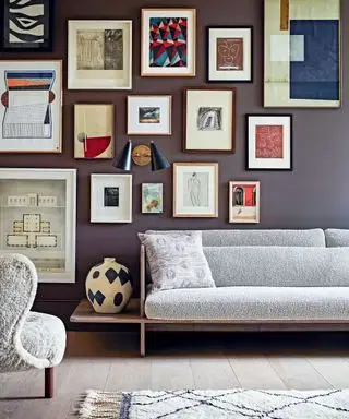 Wohnzimmer mit Sofa und Stuhl, Teppich auf Holzdielen und einer Galeriewand voller Kunstwerke.