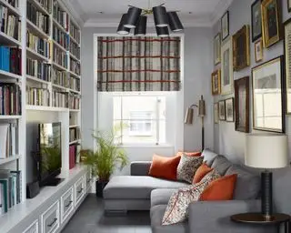 Ein gemütlicher Raum mit einer Wand aus Bücherregalen, einer Galeriewand und einem grauen Ecksofa mit orangefarbenen Kissen