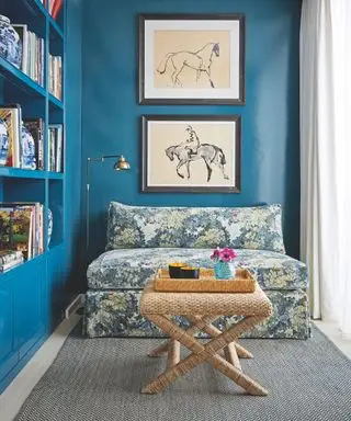 Ausgestattete Bücherregale mit Schränken darunter, Holzboden und Teppich, blau gemustertes Sofa und Zeichnungen von Pferden an einer blauen Wand.