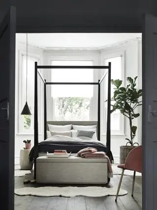 camera da letto bianca con letto grigio, pouf grigio, cornice a baldacchino nera, sospensione nera, albero di fico, poltrona, accenti corallo
