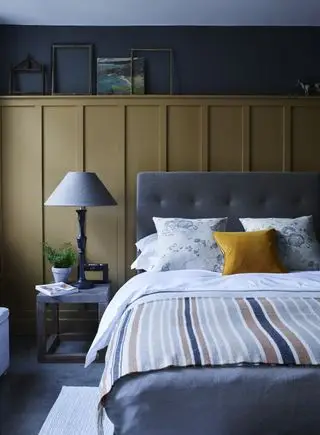 camera da letto con combinazione di colori grigio e senape, testiera del letto imbottita, pannelli, tavolino, opere d'arte, coperta a righe
