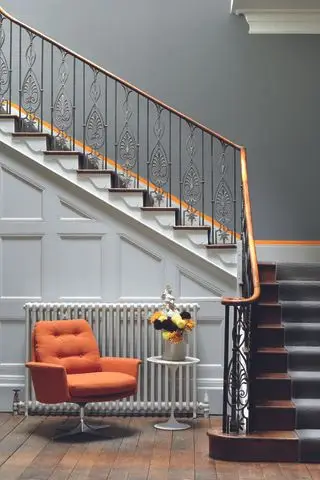 corridoio con pareti grigie e bianche, scala, accenti arancioni, pavimento in legno, poltrona arancione, tavolino