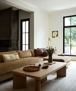 Sala de estar neutra con sofá marrón pálido y chimenea de mármol oscuro