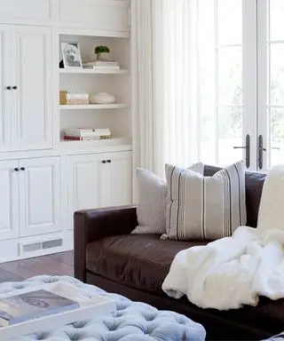 Esquina de una sala de estar blanca con un sofá de cuero marrón y un futón azul pálido