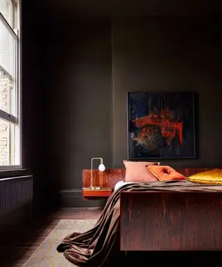 Dormitorio marrón con almohadas naranjas, paredes pintadas de marrón y suelos de madera