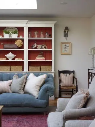 stue med blå sofa og grå lænestol med hvide udstillingsreoler med rød panel