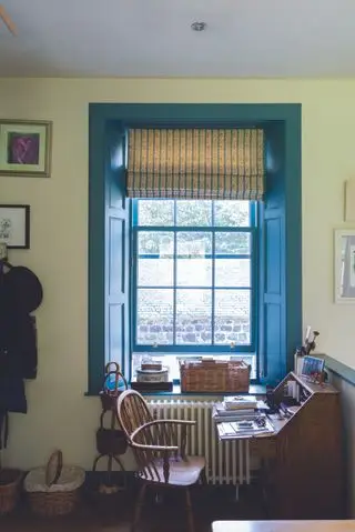 escritório doméstico amarelo com carpintaria pintada de azul e persiana com listras no peitoril da janela