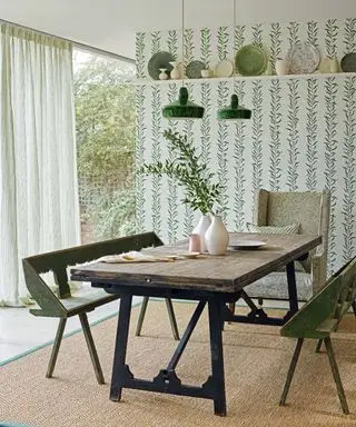 Esszimmer mit floraler grüner Tapete, Regal mit Dekorationsgegenständen und Tellern, Esstisch und Stühlen aus Holz