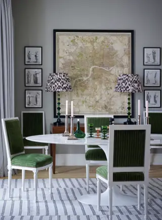 Entspannter Esszimmerbereich mit weiß gestrichenen Wänden, dunklem Holzboden, eingelassenen, bogenförmigen Regalflächen, dekoriert mit einzigartigen Ornamenten und Objekten, einer an der Wand montierten Bank mit gepolsterter Rückenlehne, zwei Esszimmerstühlen mit Gurtband, schwarzem Metallgestell und cremefarbenen Kissen