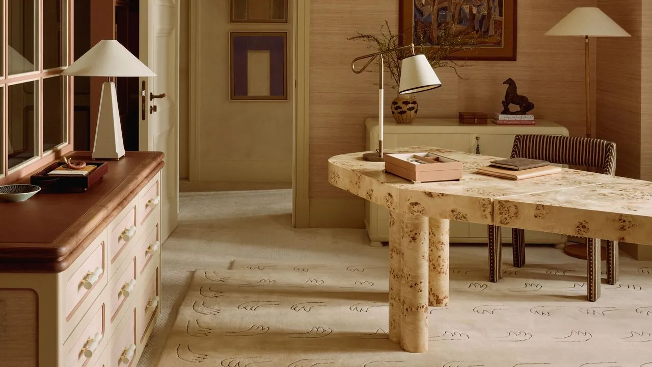 Neutral kontorplads med asymmetrisk burl træ wesk linned-skygge bordlamper vægkunst et figurelt motiv beige tæppe og en stribet kontorstol.' loading='lazy' title=