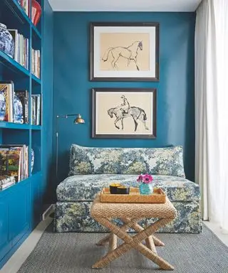 Ausgestattete Bücherregale mit Schränken darunter, Holzboden und Teppich, blau gemustertes Sofa und Zeichnungen von Pferden an einer blauen Wand.