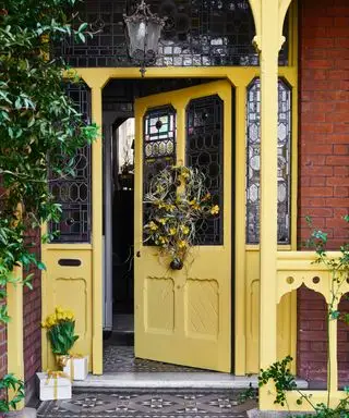 Porche de la puerta de entrada amarilla con corona de primavera, linterna tradicional, vidrieras y azulejos estampados