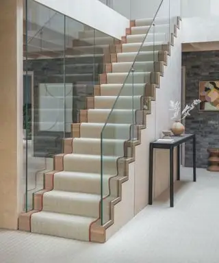 Tapete creme na escada de madeira, corredor com carpete combinando, mesa console preta.