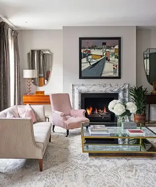 Sala de estar moderna com lareira em mármore, carpete estampado, poltronas, sofá, mesa de centro e obras de arte acima da lareira.
