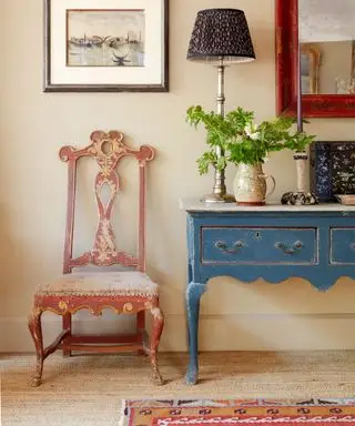 Entrada aconchegante com carpete texturizado, tapete estampado vermelho, console azul, cadeira antiquada, obras de arte e espelho na parede
