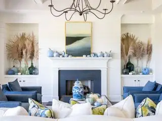 Wohnzimmer mit blau bemalten Kürbissen auf dem Kaminsims, Pampas in farbigen Glasvasen in Nischen, blauen Sesseln, Gemälde auf dem Kaminsims, Couchtisch mit Kürbissen