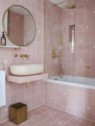 banheiro rosa com azulejos quadrados rosa, luminárias e acessórios dourados, pia flutuante