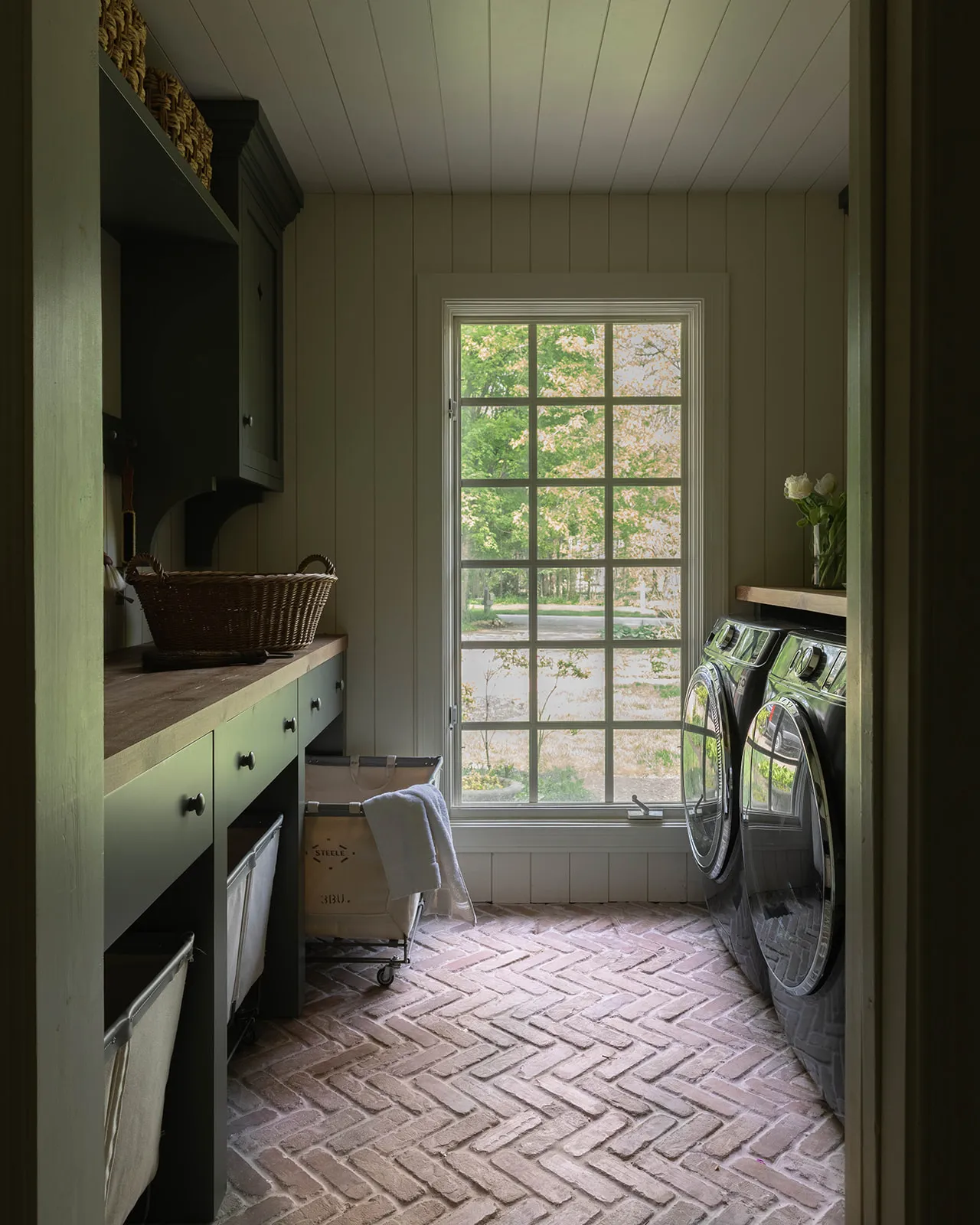 House Seven Design Laudry Room with Dark Cabinetry. Terracotta gulv og vaskeri vogner under benkeplate' loading='lazy' title=