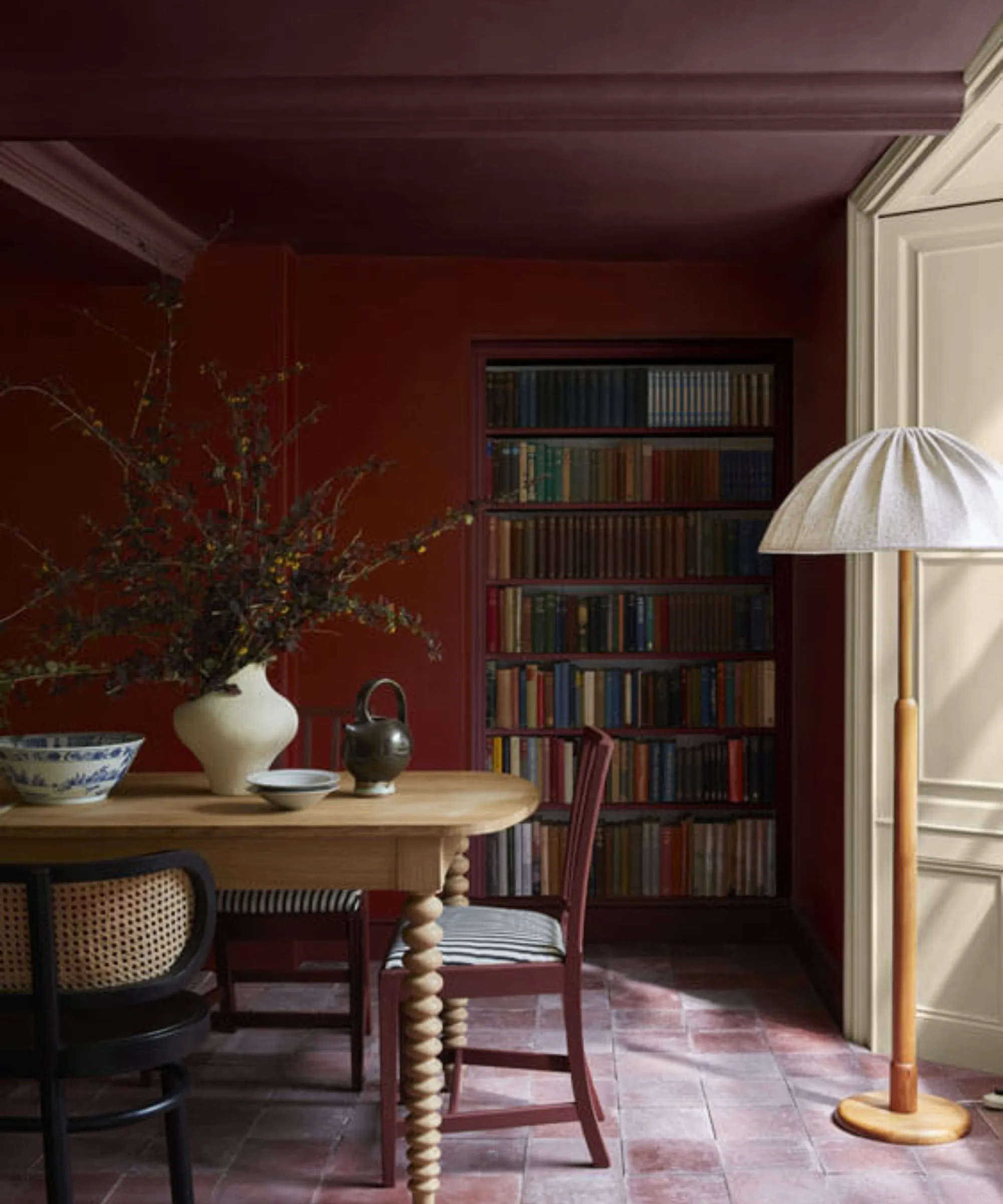 Fargegjennomvåt rød spisestue med spisebord i tre og dekorert med en vase med høstløvverk og en trelampe med hvit skjerm' loading='lazy' title=