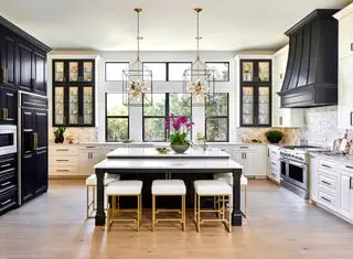 Grande cuisine avec armoires sombres et blanches, îlot central, luminaires suspendus et plancher de bois