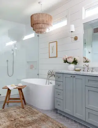 Salle de bain avec vanité grise, baignoire et douche autoportantes, tabouret et lustre