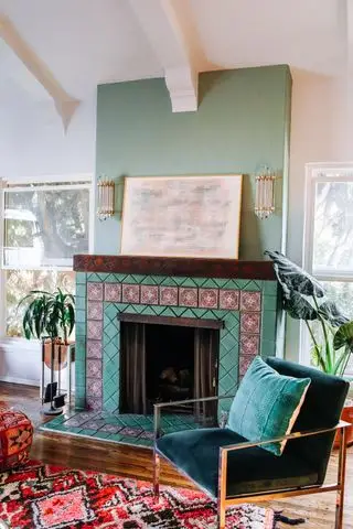 Salon avec appliques au-dessus du manteau sur cheminée verte, fauteuil, tapis et parquet