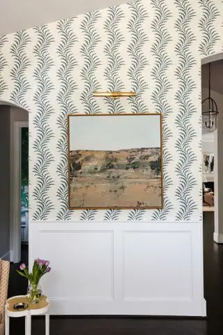 Entrée avec papier peint à motifs, œuvres d'art avec lumière au-dessus et lambris blanc en dessous