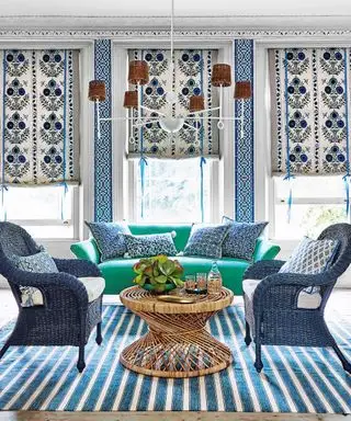 Un salon avec des tissus d'ameublement bleus et blancs, des fauteuils bleus, un canapé vert et un lustre bas
