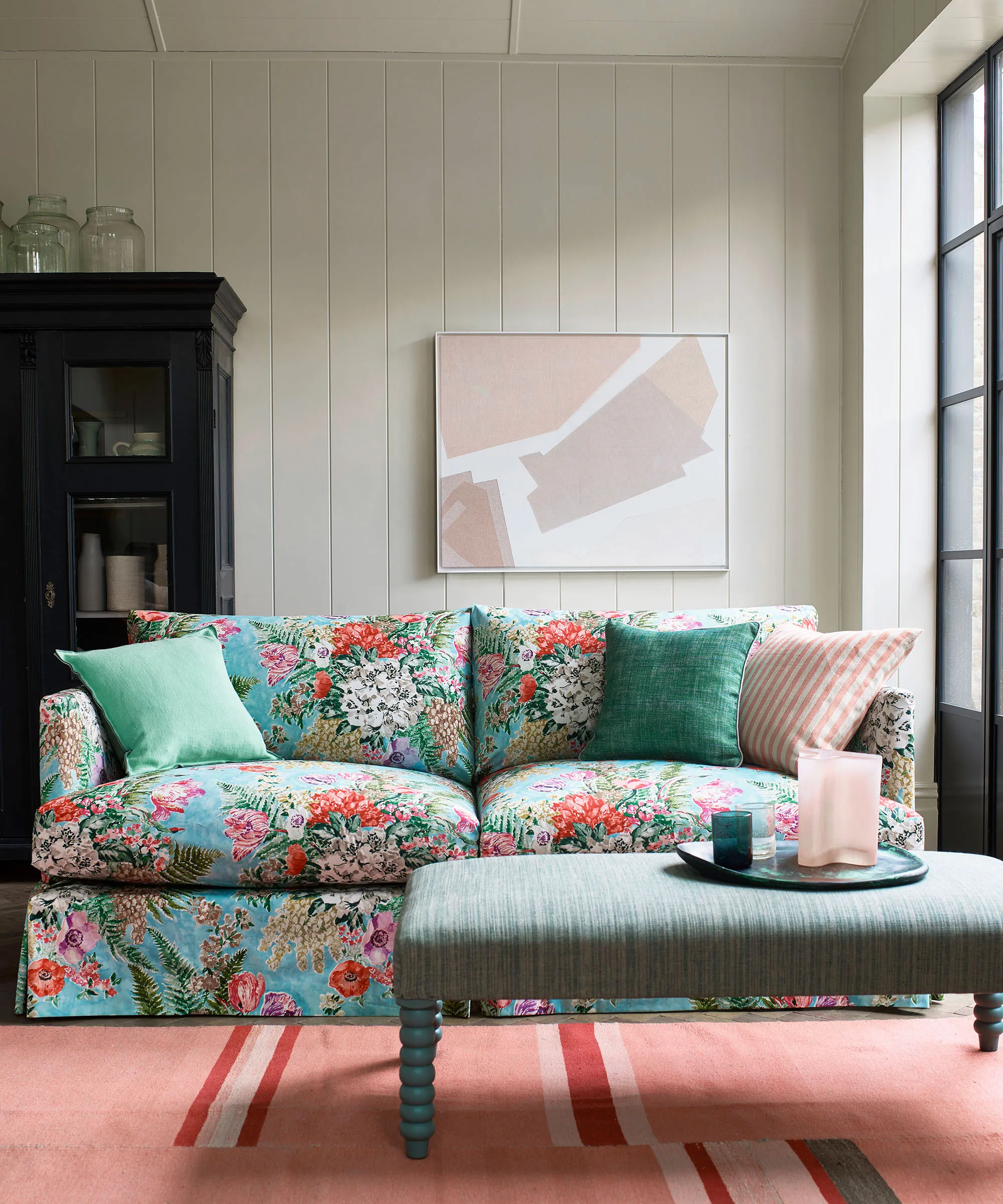 stue med blå blomstersofa rosa teppe og svart skap og kunstverk' loading='lazy' title=