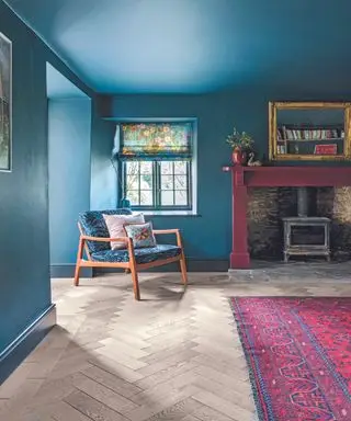 Wohnzimmer mit blau gestrichenen Wänden und Kamin, Loungesessel neben rosa Teppich