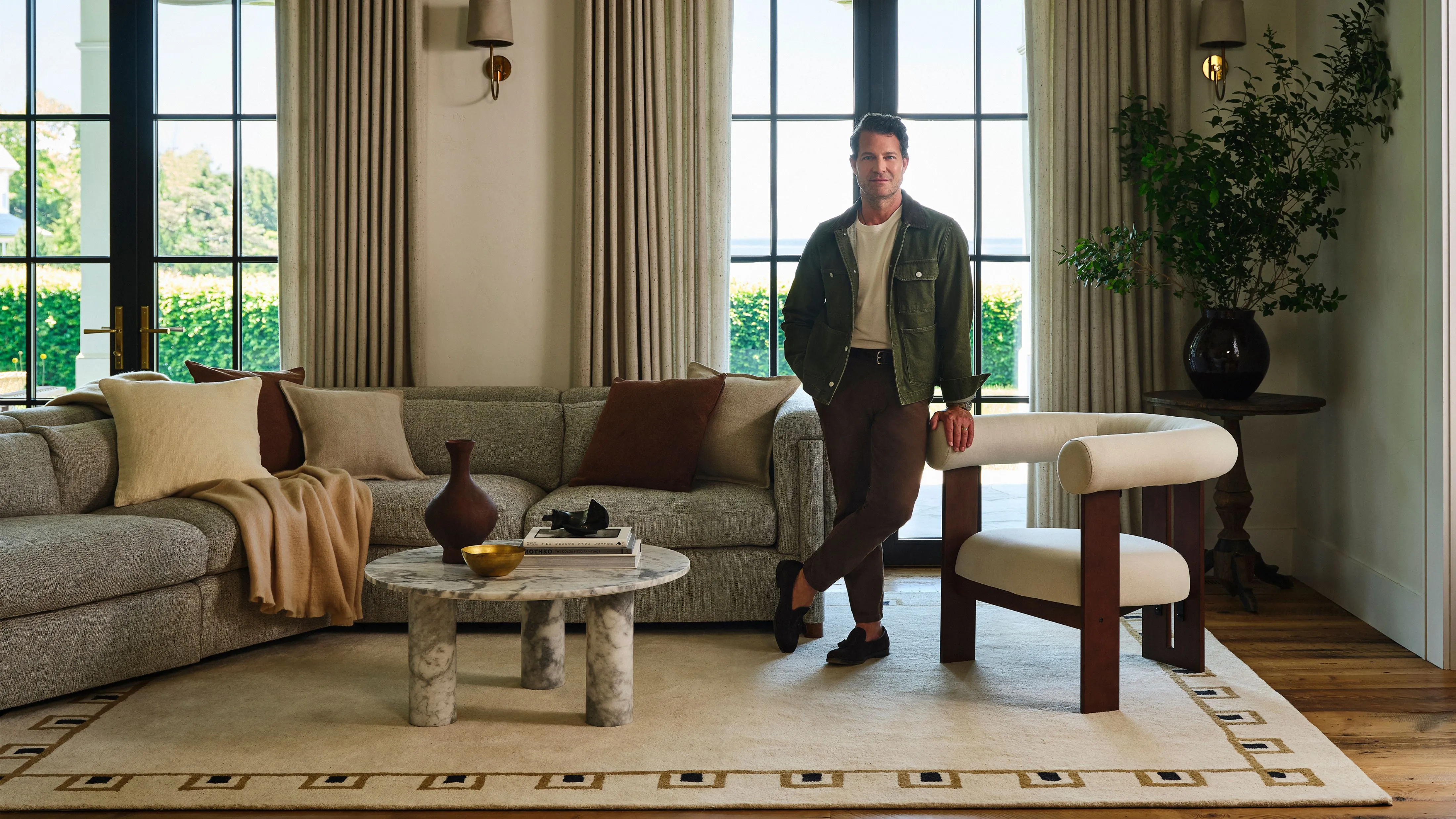 Nate Berkus de pie encima de una alfombra color crema con bordes geométricos de su nueva colaboración con Rugs USA' loading='lazy' title=