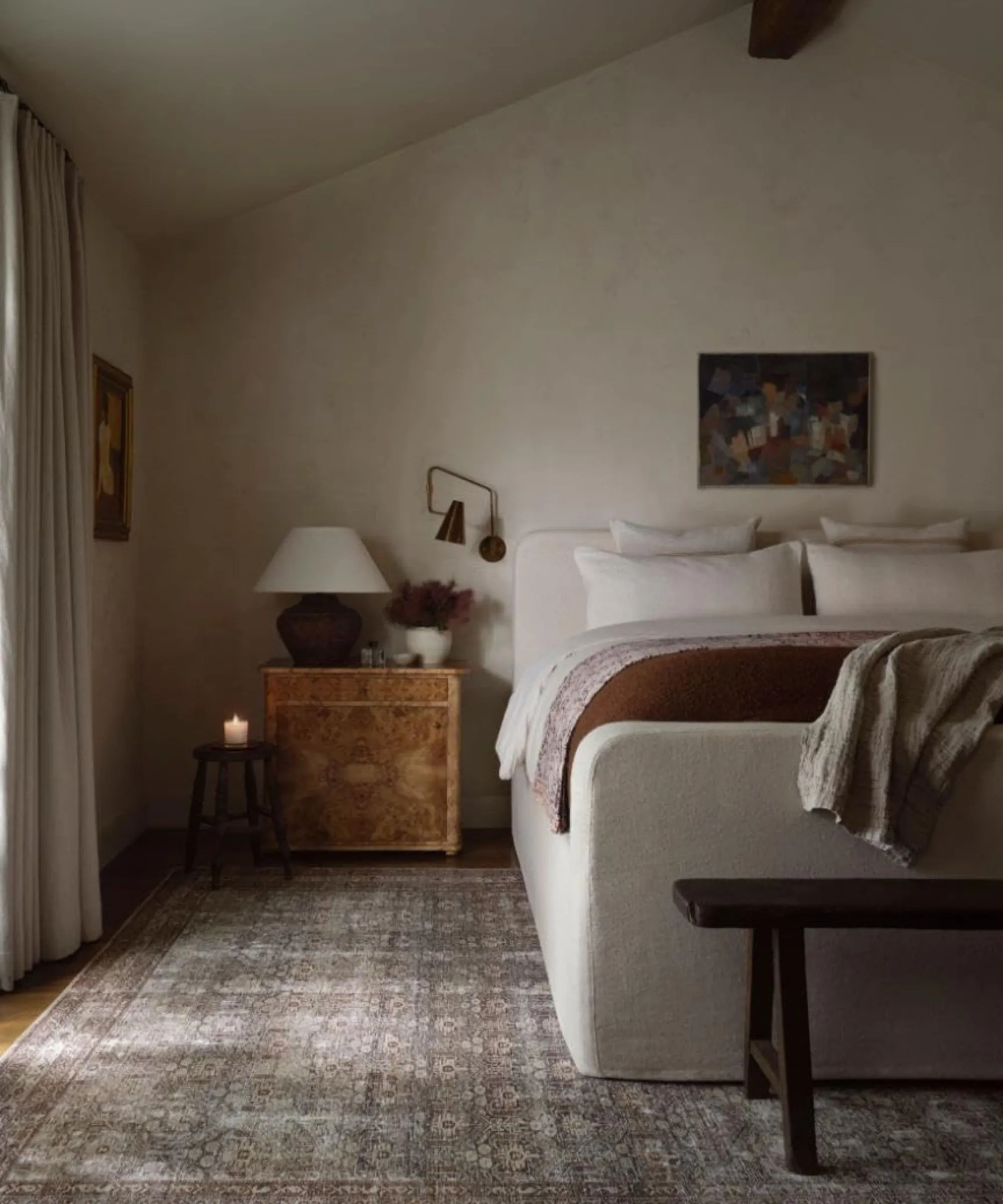 Dormitorio de estilo vintage con una cama con funda de lino, alfombra estampada gris, mesita de noche de madera y decoración vintage' loading='lazy' title=
