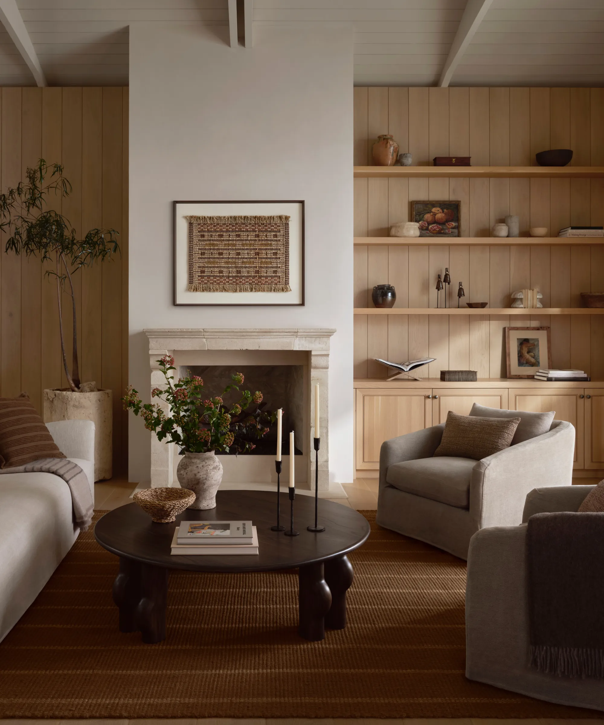 una cálida sala de estar con paneles de madera en las paredes una mesa de café redonda de madera dos sillas decorativas un sofá y una alfombra a rayas en el suelo' loading='lazy' title=