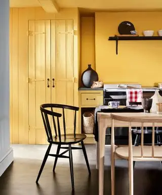 Cuisine peinte en jaune avec table à manger en bois, sol gris, étagères noires
