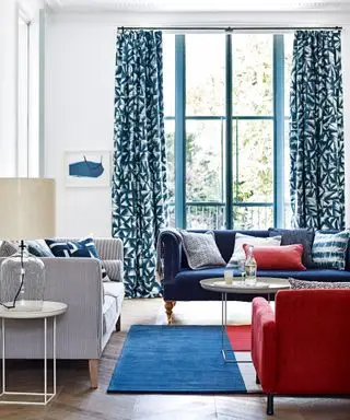 Una idea de cortina para sala de estar con paredes blancas, cortinas estampadas en azul oscuro y muebles azules y rojos.