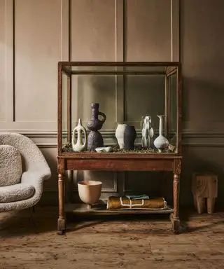 Une console en bois sur un plancher en bois contre des boiseries avec des objets sculpturaux et des vases exposés.
