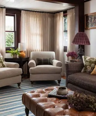 Salon chaleureux et cosy avec deux fauteuils, canapé, table basse en bois, voilages beige