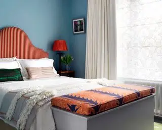 Kleine Schlafzimmer-Layout-Ideen in einem blauen Zimmer mit leuchtend orange gemustertem Kopfteil und Aufbewahrungstruhe.