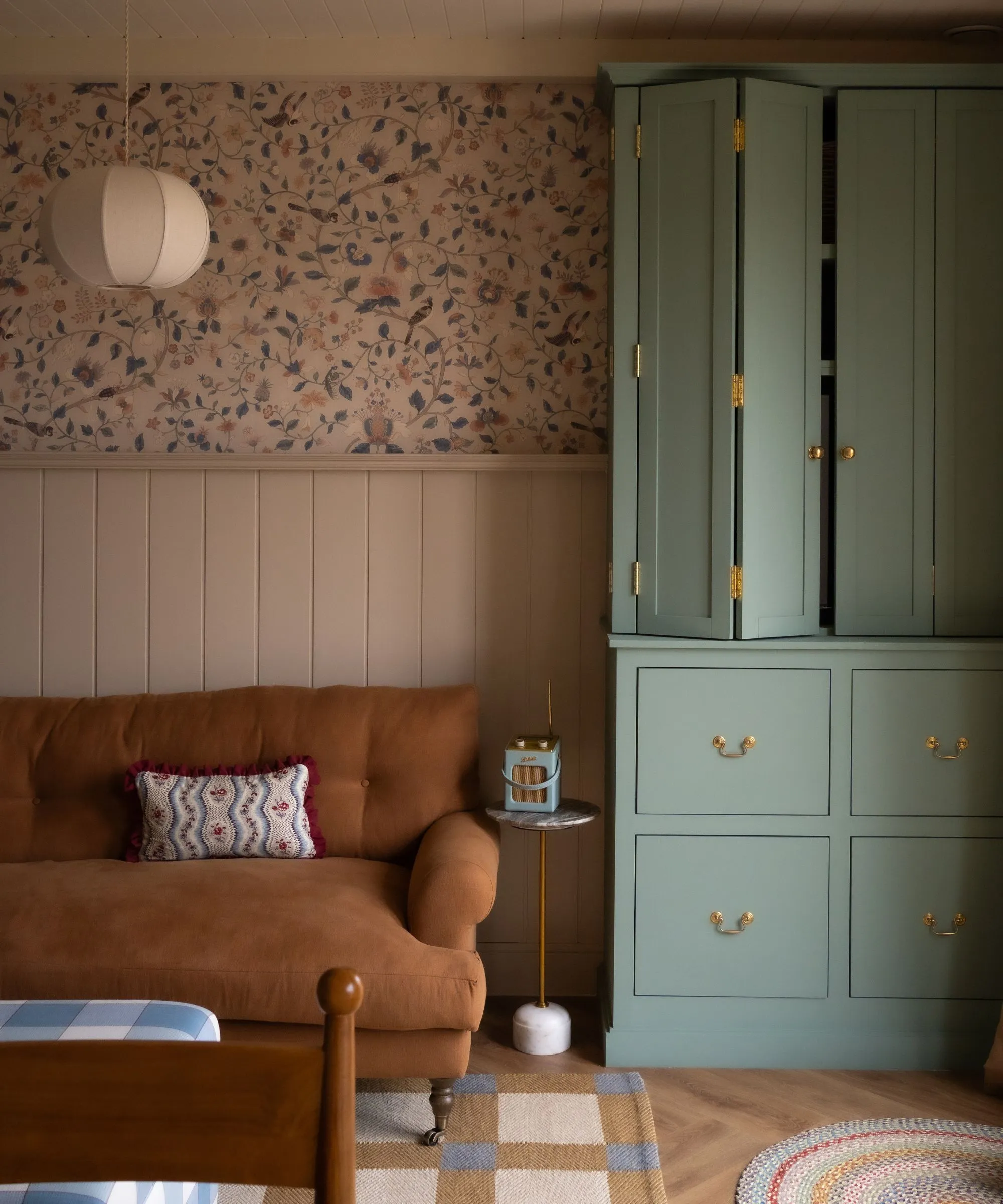 패널 벽과 반 꽃무늬 벽지가 있는 작고 아늑한 공간 황갈색 소파와 TV를 드러낼 수 있는 파란색 맞춤형 캐비닛' loading='lazy' title=
