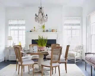 En hvit spisestue med spisebord og stoler med bordet dekket til et påskemåltid med en skål med påskeliljer som midtpunkt.