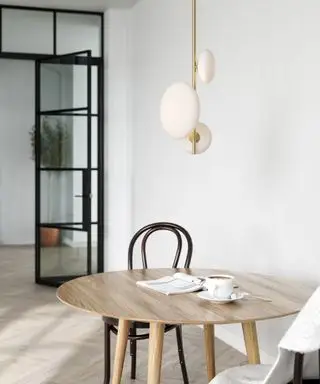 Rolig spisestue med lavthengende opal og metallisk anheng over lyst tre, rundt spisebord, svart spisestol, hvitmalte vegger, gråbeige tregulv
