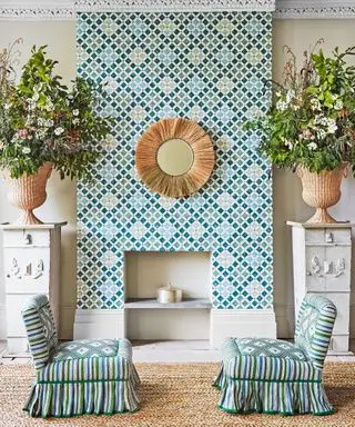 Chimenea empapelada de colores, dos sillas estampadas y jarrones de flores.