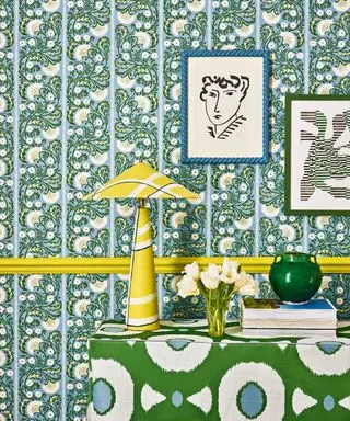 Blåt og hvidt blomstret tapet, gul kant, gul bordlampe, grøn og hvid blomstret skænk dekoreret med bøger og ornamenter