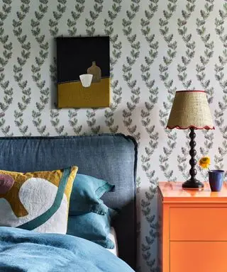 Soveværelse med grønt blomstertapet, orange sidebord, lampe, blå seng