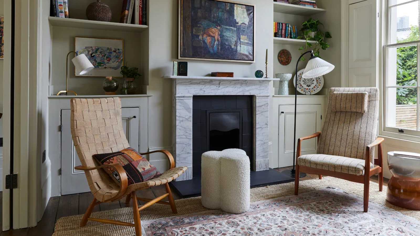 小さな暖炉の周りに作り付けの棚があるリビングルーム、アクセントチェア 2 脚、ブークレのスツール、地面に置かれたヴィンテージ風のペルシャ絨毯' loading='lazy' title=