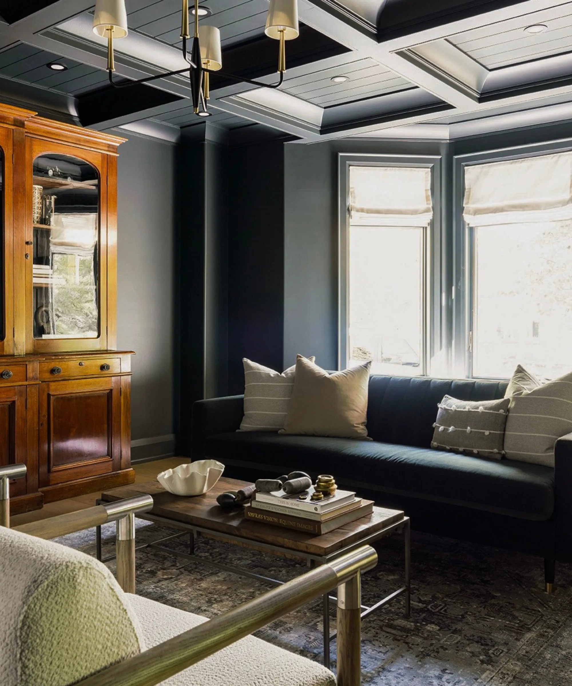 暗いリビングルーム、枕がいくつかある深い青色のソファ、本と装身具が置かれたコーヒーテーブル、大きな木製のキャビネット、床にはペルシャ絨毯が敷かれています。' loading='lazy' title=