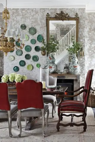 Wallaper estilo damasco en el comedor con mesa, espejo ornamentado, platos en la pared, lámpara de araña dorada, sillas de comedor tapizadas
