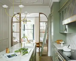 Cocina con puerta arqueada de madera, superficies de mármol, isla y gabinetes verdes.