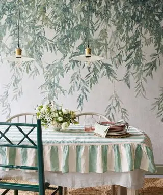 comedor con papel tapiz botánico frondoso y mantel de rayas verdes con silla verde y luces colgantes